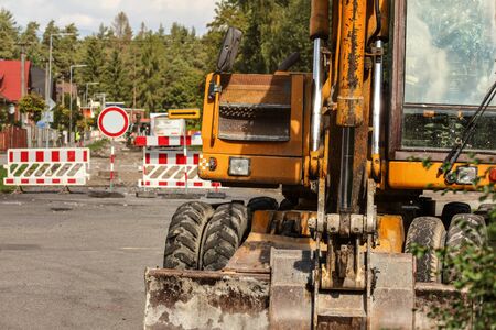 Detail on old yellow digger machine back, driver cabin visible, road closed signs, digged ground and...