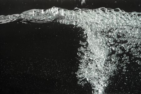 Water splashing as it's poured into aquarium tank, black background.