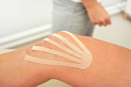 Kinesiology tape in body color cut to thin stripes applied to knee of female patient, closeup detailの写真素材