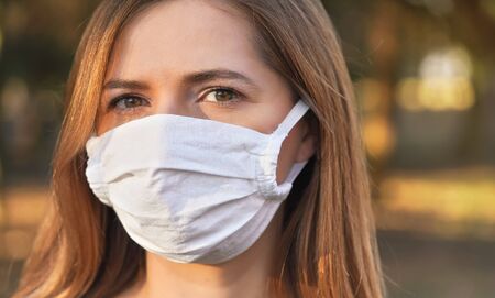 Young woman wearing white cotton virus mouth nose mask, nice bokeh in background, closeup face...