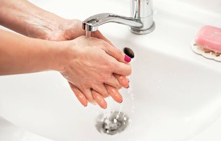 Young woman washing her hands under water tap faucet with soap. Detail on liquid over skin. personal hygiene concept.の写真素材
