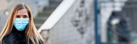 Young woman wearing disposable blue virus face mouth nose mask, closeup portrait, banner with blurred background space for text right side. Coronavirus covid-19 outbreak prevention conceptの写真素材