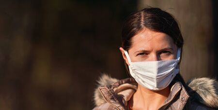 Young woman wearing white cotton home made virus mouth nose mask in park, wide banner, space for text left sideの写真素材