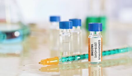Coronavirus covid-19 vaccine concept -  small bottle with blue cap on glossy white desk, green...