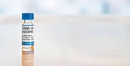 Coronavirus Covid-19 vaccine concept - small glass vial with blue caps on white table, closeup detail wide banner space for text right side (sticker is own design  with dummy data, not a real product)の写真素材