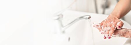Young woman washing her hands under water tap faucet with soap, nails covered purple polish. Wide...