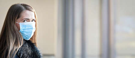 Young woman wearing disposable single use blue virus face mouth nose mask, closeup portrait, banner with space for text right side. Coronavirus covid-19 outbreak prevention conceptの写真素材