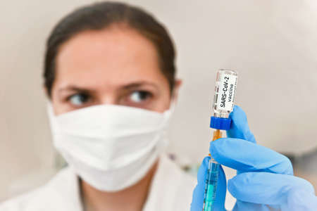 Coronavirus vaccine (label own design, not real product) injected into syringe hold by hand with...