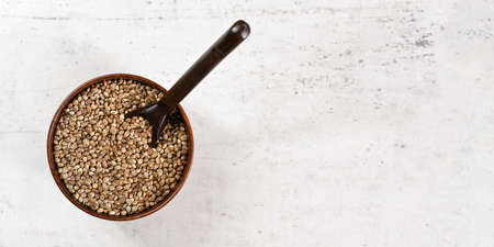 Unpeeled hemp - Cannabis sativa - in small dark wooden cup with spoon view from above, white stone...