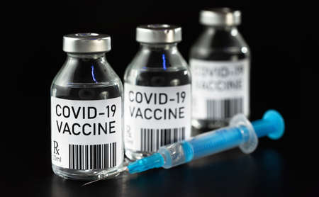 Coronavirus Covid-19 vaccine concept -  three glass vials on black table, blue syringe near closeup detail (own design - dummy bar code)の写真素材