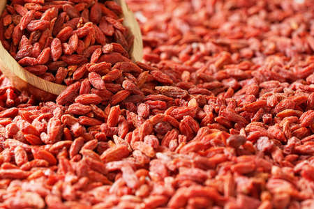 Dry goji berries in small wooden bowl, scattered on desk below
