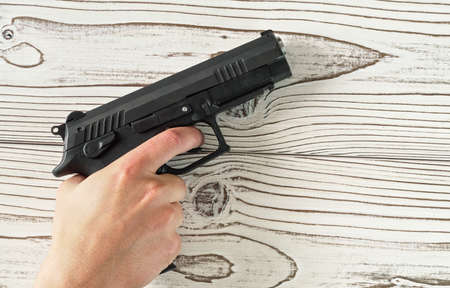 Man hand holding black modern metal gun on white wooden table, closeup detail