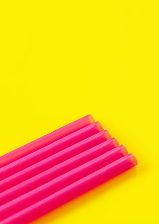 Six pink plastic drinking straws on yellow board, forming diagonal line - abstract closeup detail, space for text aboveの写真素材