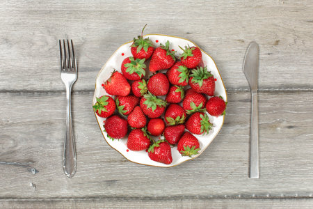 Tabletop view, plate with strawberries on gray wood boards desk, fork and knife next to it - ready to eat healthy snack concept.の写真素材