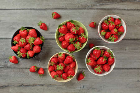 Tabletop view, small bowls with strawberries, some of them spilled on gray wood desk.の写真素材