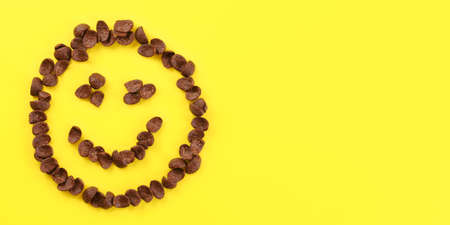 Tabletop view, smiley face made of brow chocolate corn flakes on yellow board. Space for text on right side.の写真素材