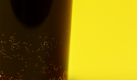 Small bubbles in dark fizzy drink, closeup detail with yellow backgroundの写真素材
