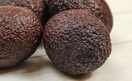 Detail of ripe whole brown avocado, rough skin visible, more avocados on white boards in background.