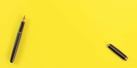 Top down view - black fountain ink pen with gold nib, opened, cap on the right, yellow background, space for text.の写真素材