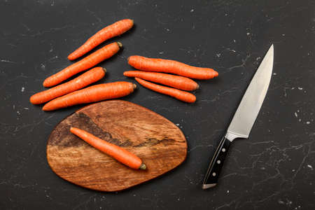 Top down view, orange carrot, chopping board and chef knife next to it, on black marble board.の写真素材