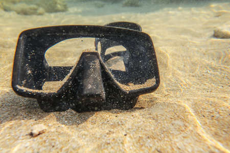 Underwater photo - black diving mask / goggles on sand in shallow water near beach.の写真素材