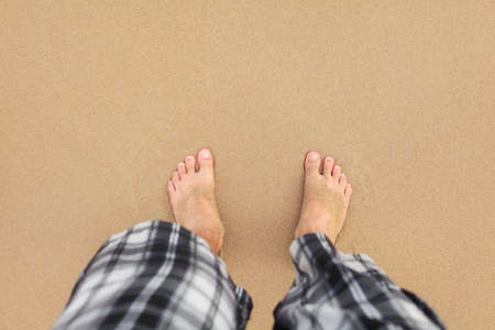 Top down view, man wearing black and white shorts feet in wet sand on beach. Space for text upper part.の写真素材