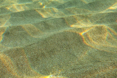 Underwater photo - sun shining on sand "dunes" in shallow water, casting small "rainbows". Abstract marine background.の写真素材