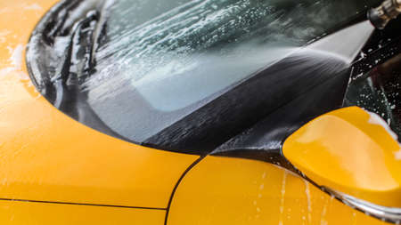 Detail of yellow car front window washed in self serve carwash, water spraying from high pressure nozzle.の写真素材