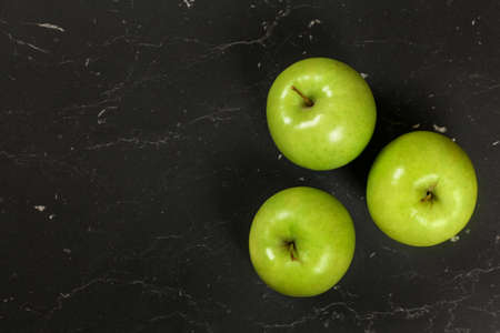 Overhead shot - three green apples on black board, space for text on left side.