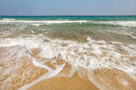 Sand on the beach wet from small waves; azure sea ad clear sky in backgroundの写真素材