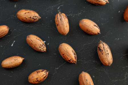 Overhead photo - spotted whole pecan nuts ( Carya illinoinensis ) on black marble like working...