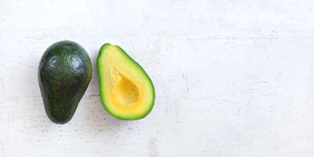 Overhead shot - avocados, one cut in half on white working board. Wide banner with space for text right.の写真素材