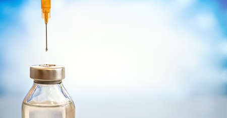 Injection syringe needle with drop of liquid above glass vaccine bottle, closeup detail space for text right sideの写真素材