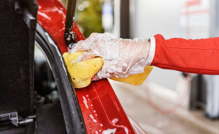 Young woman cleaning rear part of her car, closeup detail on hand in glove holding yellow sponge