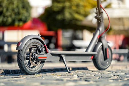 Electric scooter parked on tiled cobblestone pavement - closeup detail on rear wheel with disc brakeの写真素材