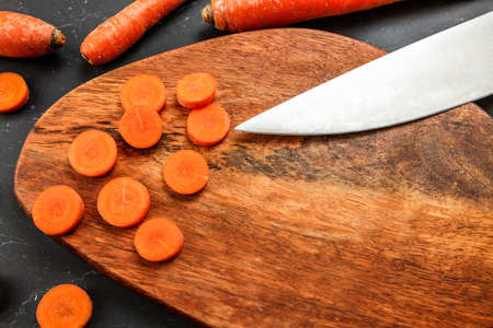 Wooden cutting board (space for text) with carrot sliced to small circles, blade of chef knife visible, view from above.の写真素材