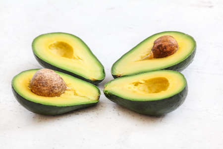 Two avocados cut in half, seed showing, on white working board.の写真素材