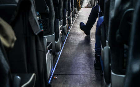 Coach bus seats seen from back row, one passenger has his foot in aisle.の写真素材