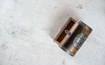 Small wooden decorated empty chest lid opened, on white stone board, photo from above