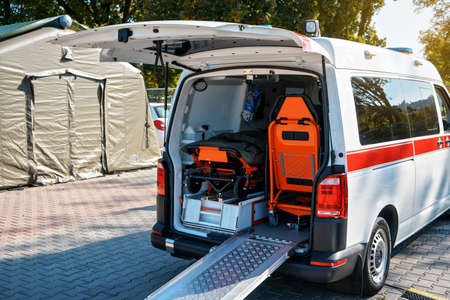Opened back door of ambulance vehicle, bright orange carrying stretcher and chair visible