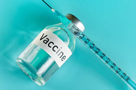 Glass vial with label vaccine and hypodermic syringe needle near, view from above on green cyan backgroundの写真素材