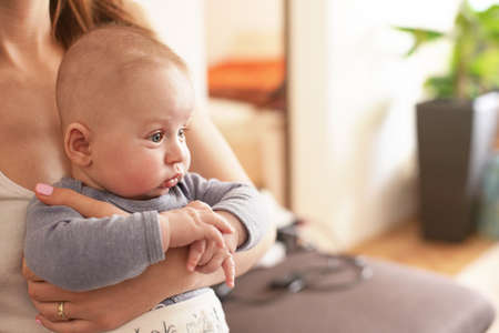 4 months old baby boy infant sitting on her mother, blurred backgroundの写真素材