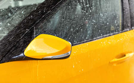Front side mirror of bright yellow car washed in self serve carwash, water spraying over glassの写真素材