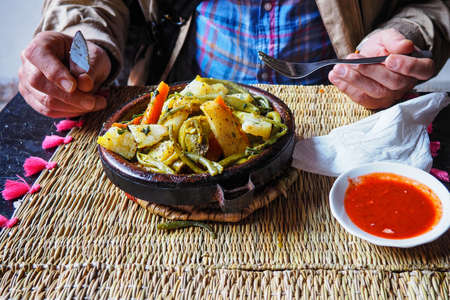 Tajine or tagine - traditional Berber dish served in earthenware bowl at typical Moroccan street restaurant, closeup detail, man hands holding fork and knife background as hes about to eatの写真素材