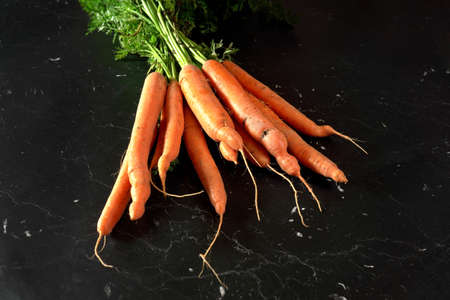Bunch of organic raw carrot with green leaves on black marble like board, view from aboveの写真素材