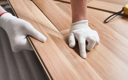Installing laminated floor, detail on man hands in white gloves positioning wooden tile, over white foam base layerの写真素材