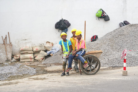 Antananarivo, Madagascar - April 24, 2019: Group of unknown Malagasy workers in hard hats and reflective jackets standing near gravel heap at construction site next to main roadのeditorial素材