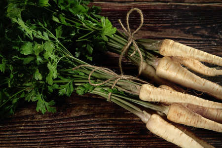 Fresh parsnip roots with green leaves on dark wooden boardの写真素材