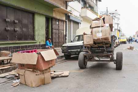 Antananarivo, Madagascar - April 24, 2019: Simple cart with empty carton boxes and wooden boards (to setup stall for morning market) pulled at main street. Unknown Malagasy man sits on floor at backのeditorial素材