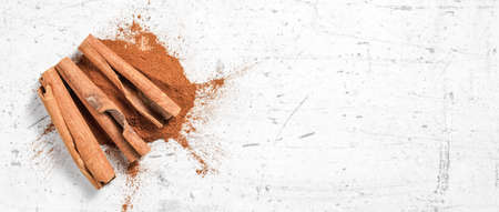 Cinnamon bark sticks and ground powder on white stone like board, wide banner - space for text right